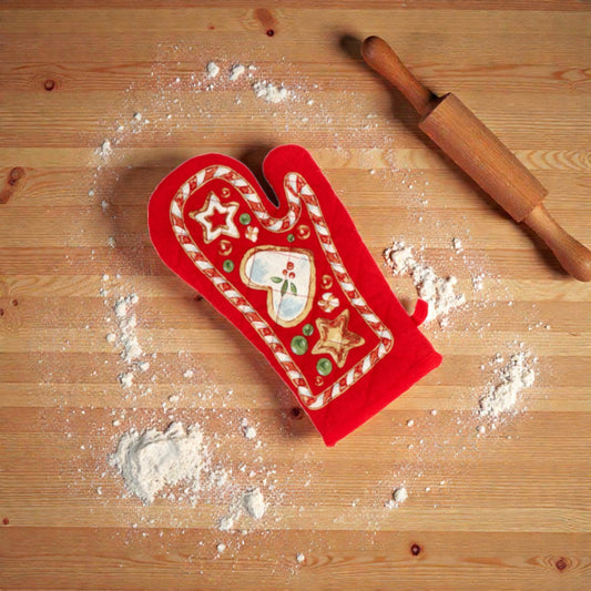 Guanto da cucina rosso a tema natalizio un piano in legno con oggetti festivi.
