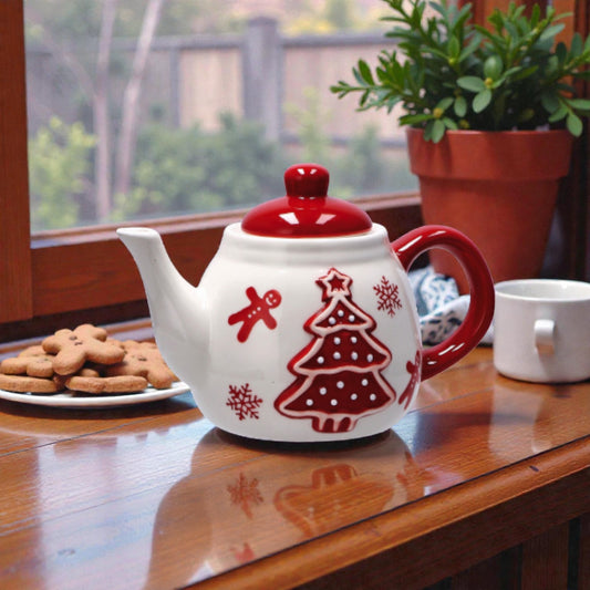 Teiera di natale in ceramica rossa e bianca con illustrazione albero di natale di marzapane, ambienta su un piano in legno in una casa festiva.