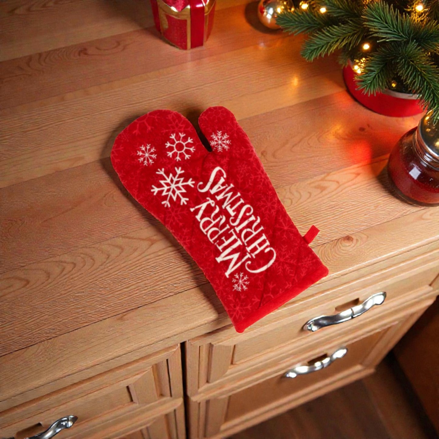 Guanto da cucina rosso a tema natalizio un piano in legno con oggetti festivi.