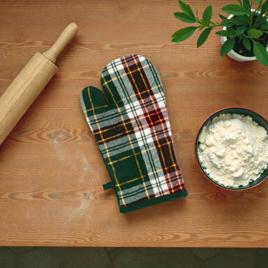 Guanto da cucina Holly in plaid a tema natalizio su un piano in legno con vicino una ciotola con farina e un mattarello in legno.