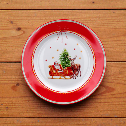 Piatto di natale bianco con righe rosse e verdi con disegno babbo natale e slitta su un piano in legno.