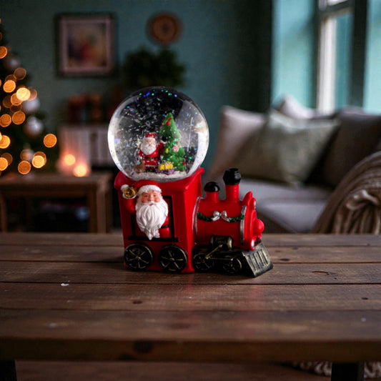 Palla di neve di Natale con base a forma di locomotiva rossa e luci LED. Ambientata in una casa festiva e accogliente.