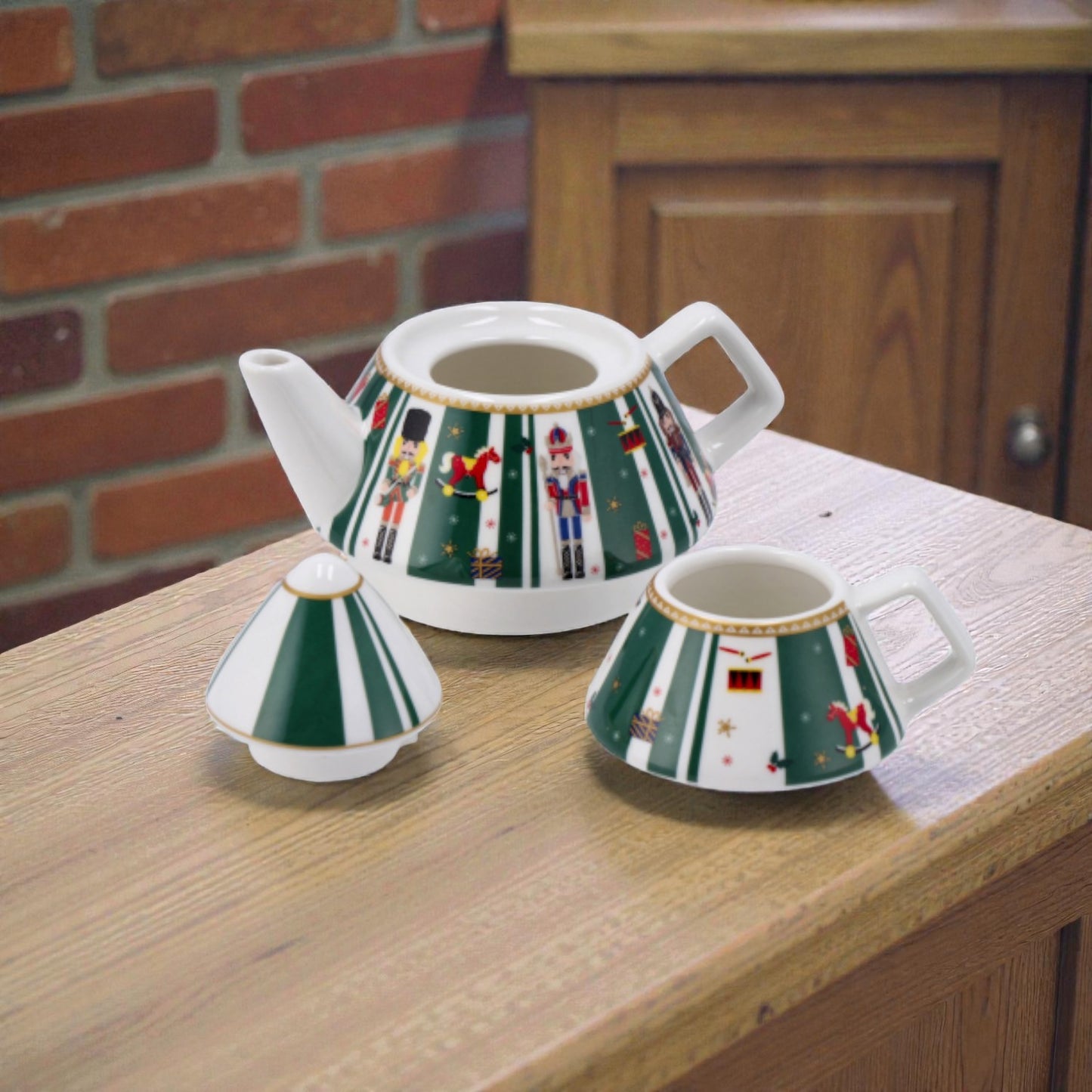 Kit teiera impilabile di natale con tazza, con illustrazioni verde e illustrazione schiaccionoci su un piano in legno, ambientato in una casa luminosa
